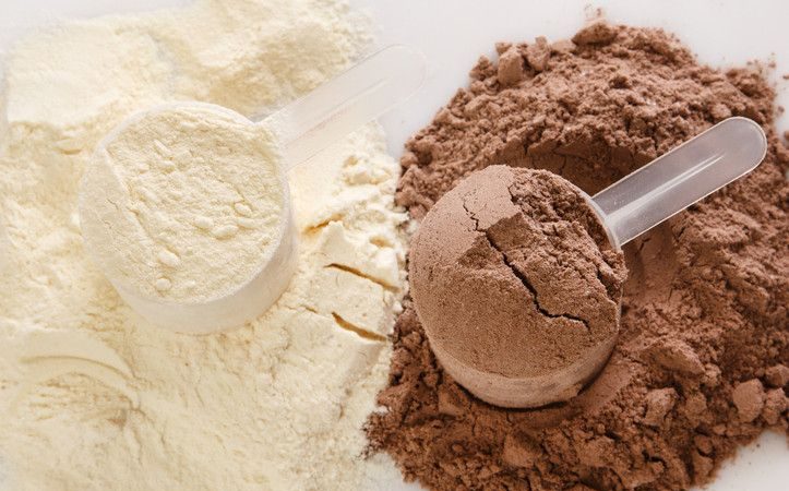 Två skopor med proteinpulver i färgerna vanilj och choklad på en vit bakgrund.
