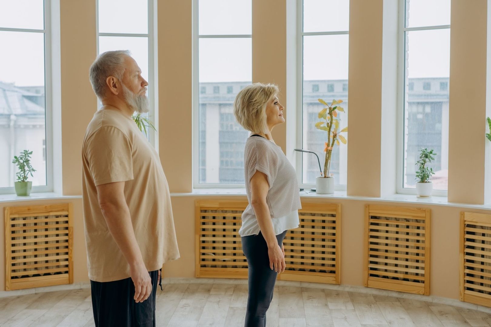 Två vuxna personer står upprätt och tränar medveten hållning inomhus