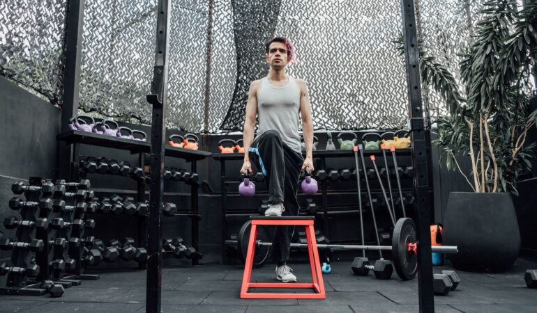 Person tränar step-up med två lila kettlebells på ett gym