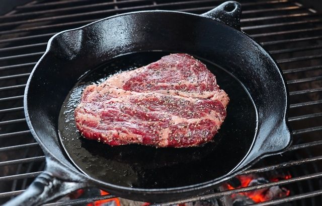 Köttbit steks i en gjutjärnspanna över glödande grillkol